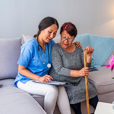 Smiling senior woman with walking stick and helpful caregiver holding her hand