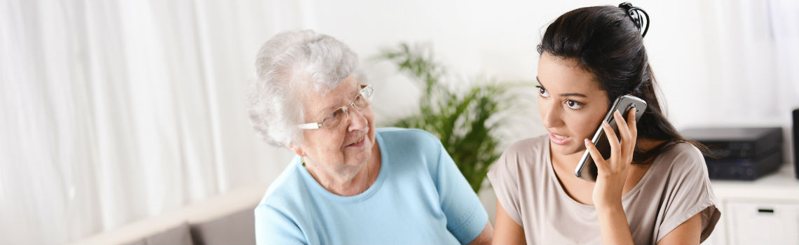 Young woman speaks on phone while elderly woman watches her