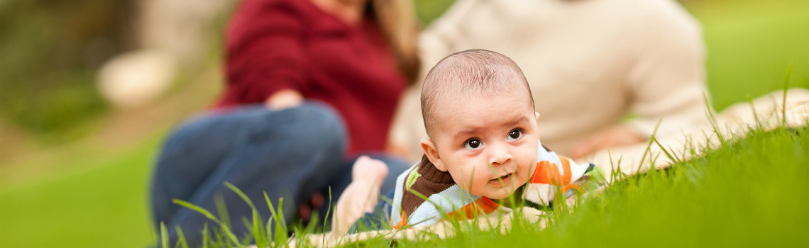 baby crawling in grass with parents watching