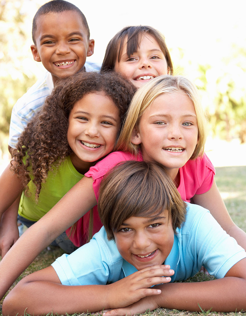 three smiling kids piled on top each other on the grass
