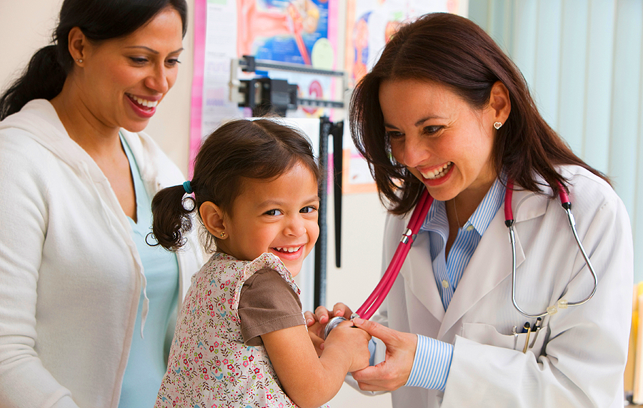 toddler laughing while doctor examines her and mom watches