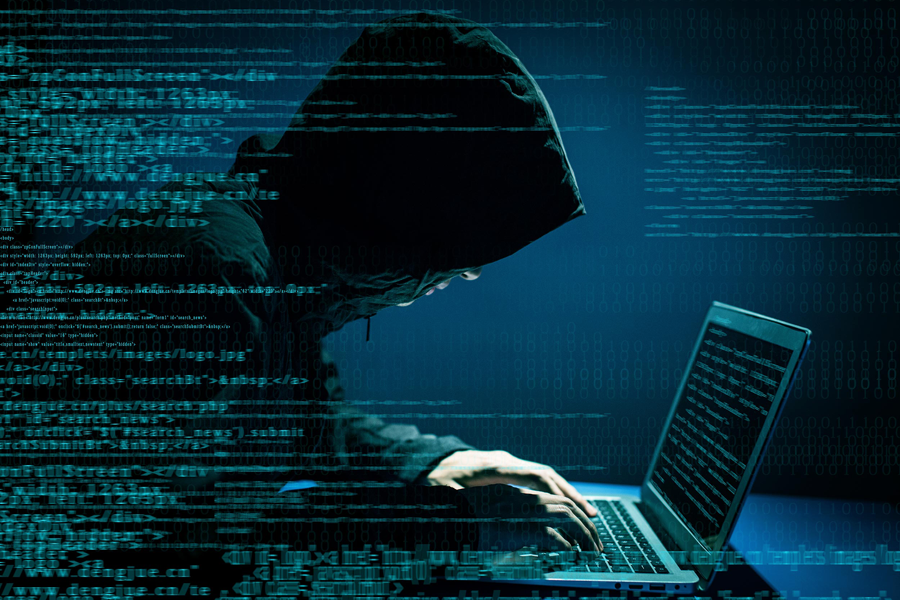 hooded figure hacking on laptop