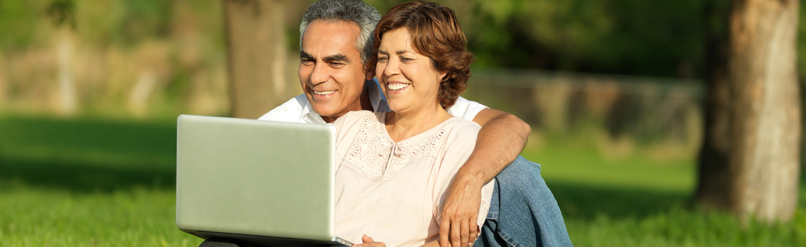 a couple sitting outside and looking at a laptop