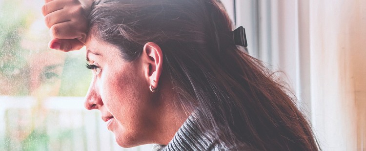 Woman looking out window with hand on forehead